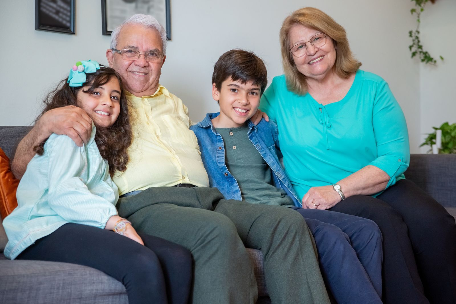 Gray-haired grandfather and grandmother smiling on a living room sofa with their two grandchildren